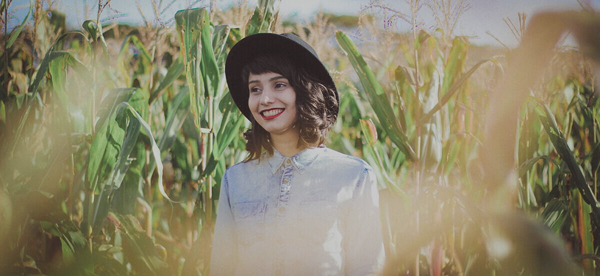Woman wearing hat walking through corn field in Spring
