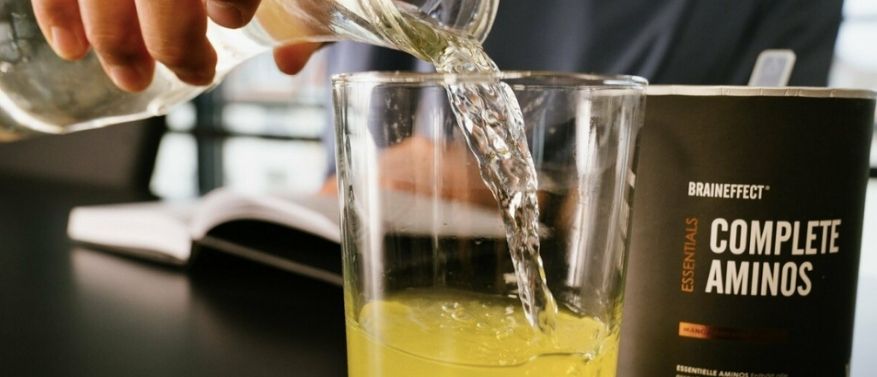 Hand schüttet Getränkepulver mit Aminosäuren von Braineffect ins Glas