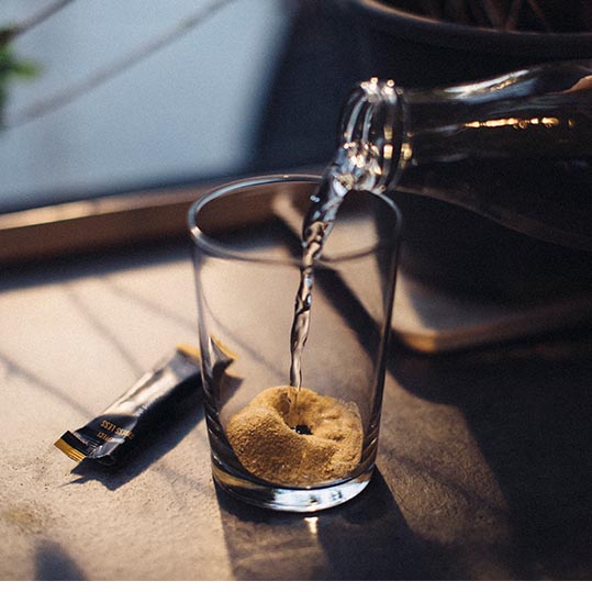 Flasche gießt Wasser in Glas mit Pulver